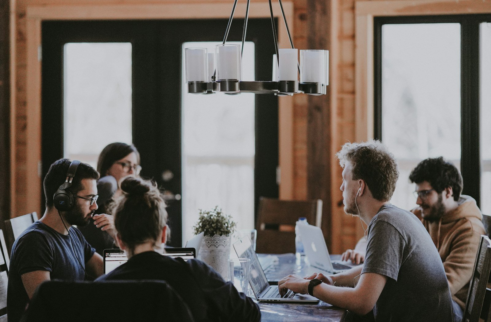 Five professionals working on laptops around a long wooden table in a bright shared workspace. Photo: Unsplash.