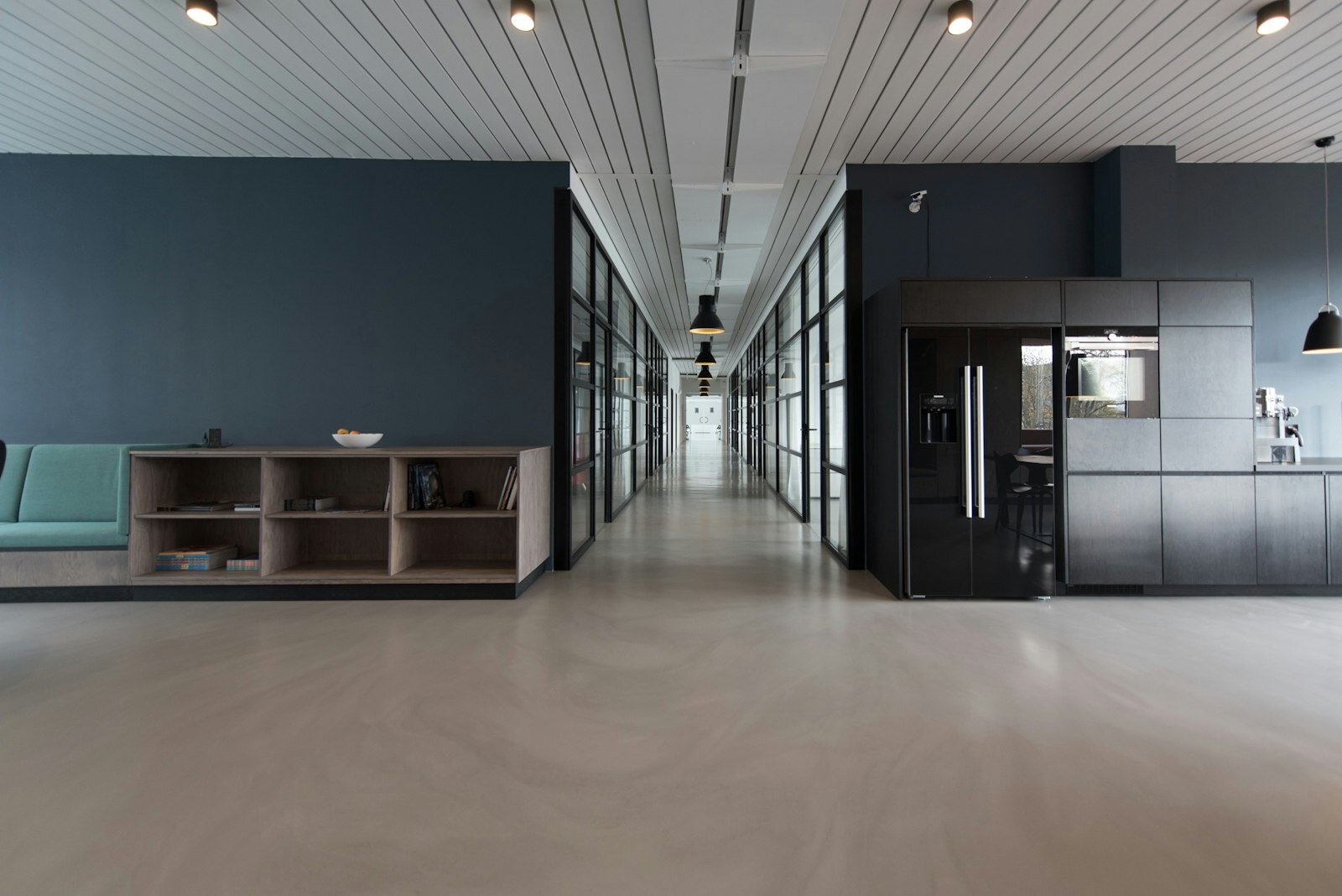 Modern glass-walled office corridor with black pendant lights and a polished concrete floor. Photo: Unsplash.
