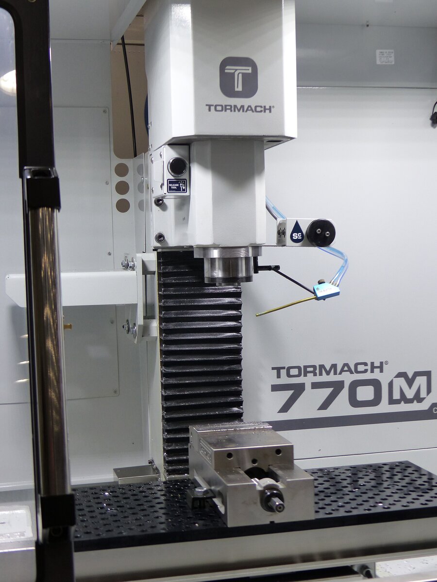 Tormach 770M CNC milling machine spindle, fixture plate, and precision vise in a clean shop. Photo: Wikimedia Commons.