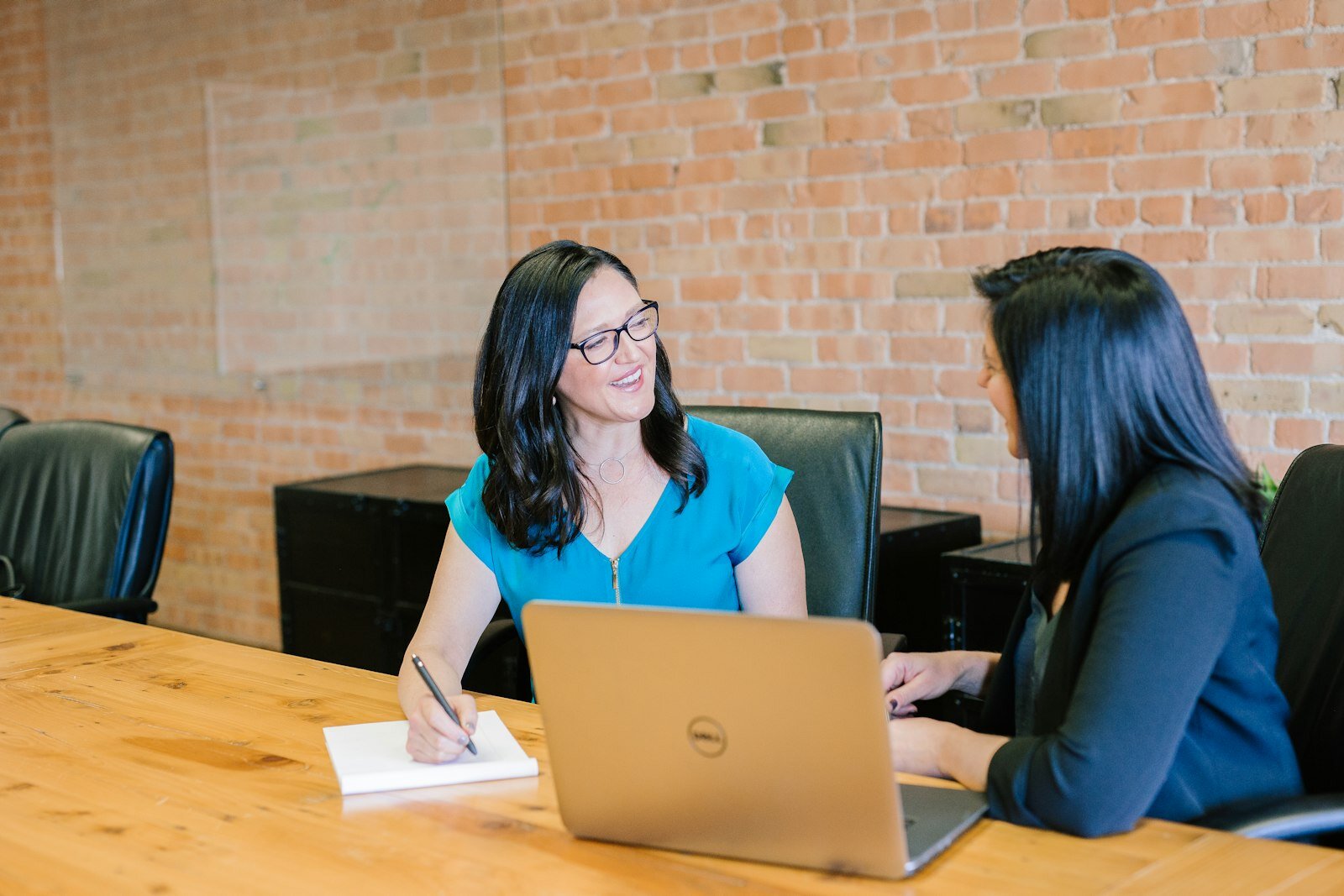 Two professionals in a sales consultation at a conference table with a laptop—the commercial handoff Koa-style CRM agents aim to accelerate with correct multi-step tool use. Photo: Unsplash.