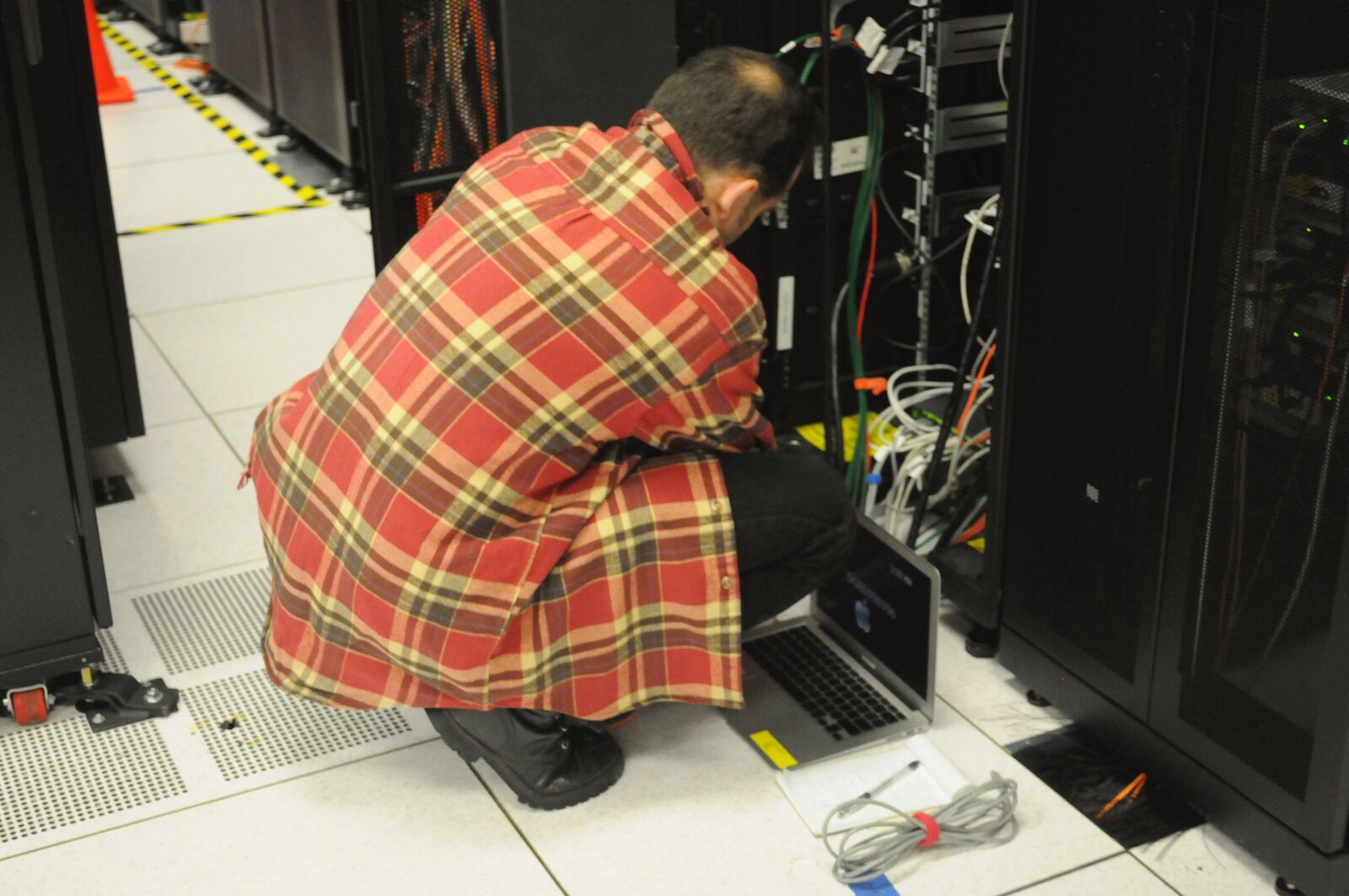 Technician with laptop working on a server rack at NERSC—field and systems service context. Photo: Wikimedia Commons.