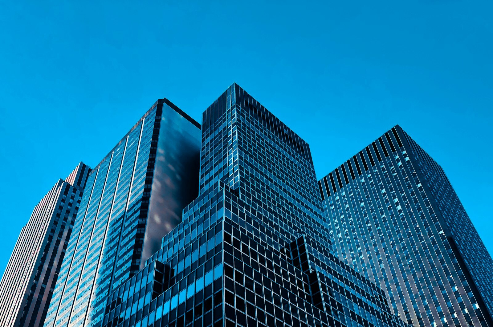 Low-angle view of modern glass office towers against a clear blue sky. Photo: Unsplash.