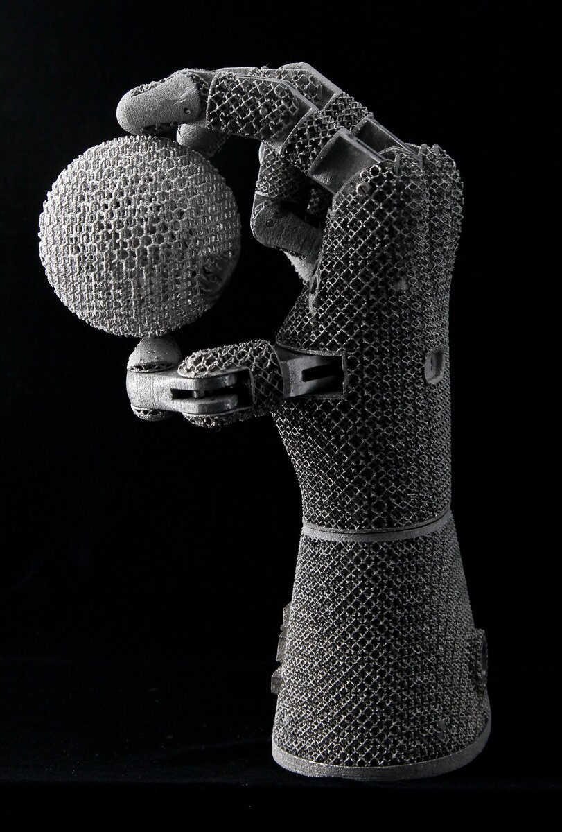 Metal additive-manufactured lattice hand holding a lattice sphere—complex geometry enabled by powder-bed fusion. Photo: Wikimedia Commons.