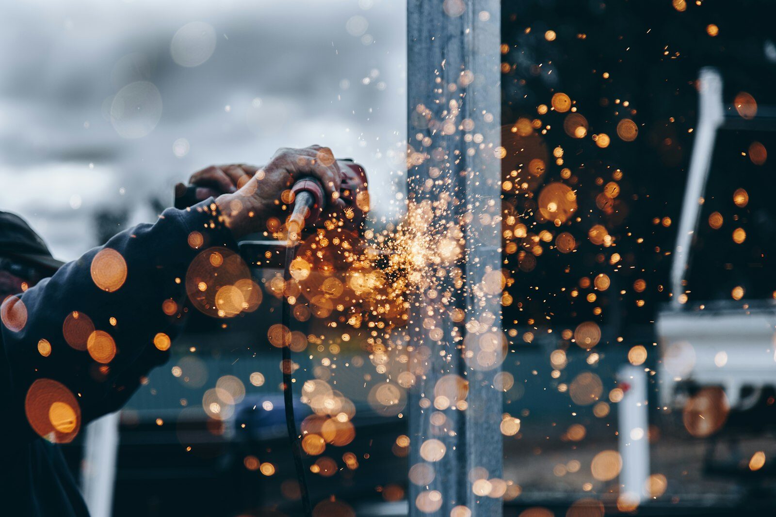Worker grinding a steel beam with a shower of orange sparks. Photo: Unsplash.