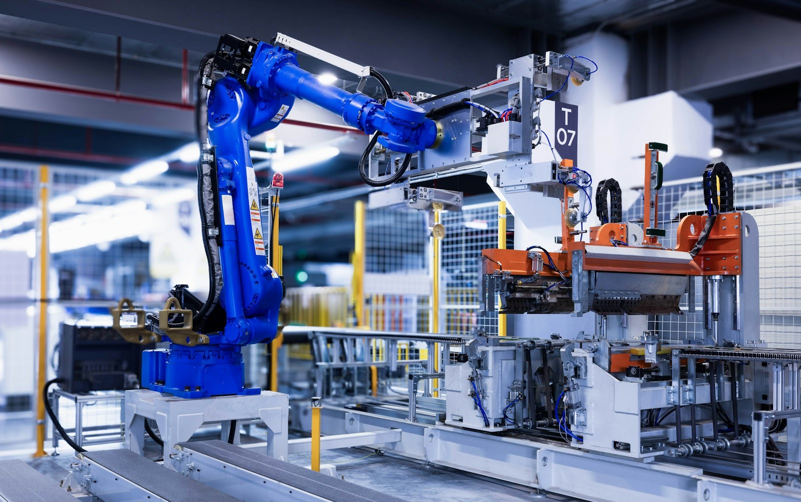 Blue industrial robot arm working an automated assembly station on a clean factory floor