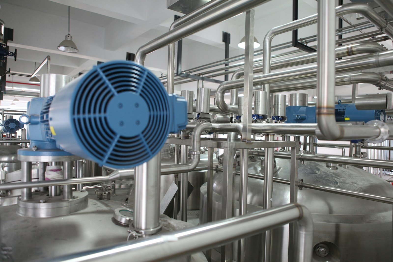 Stainless process plant with blue motors, tanks, and piping under bright industrial lighting. Photo: Unsplash.