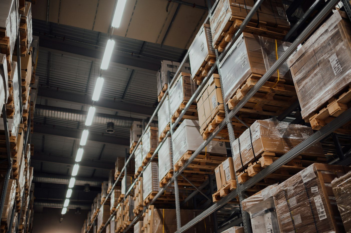 Warehouse aisle with palletized inventory on tall racks—supplier and material traceability for connected QMS. Photo: Unsplash.