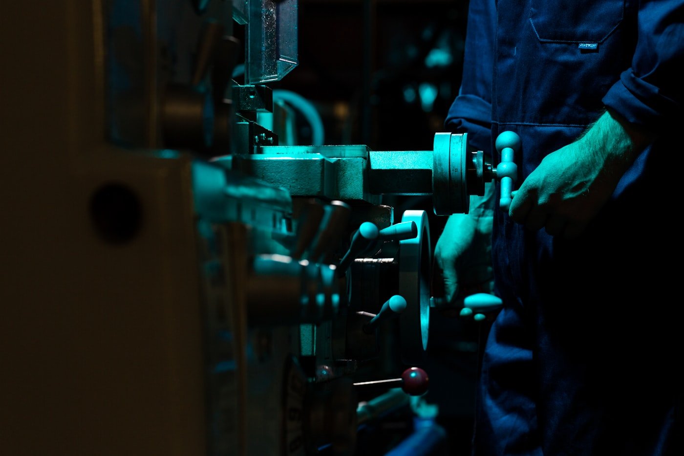 Machinist operating precision industrial machine tools under cool shop lighting. Photo: Unsplash.