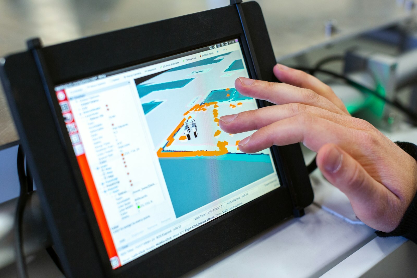 Hand interacting with an industrial HMI showing 3D robot navigation and sensor overlays. Photo: Unsplash.