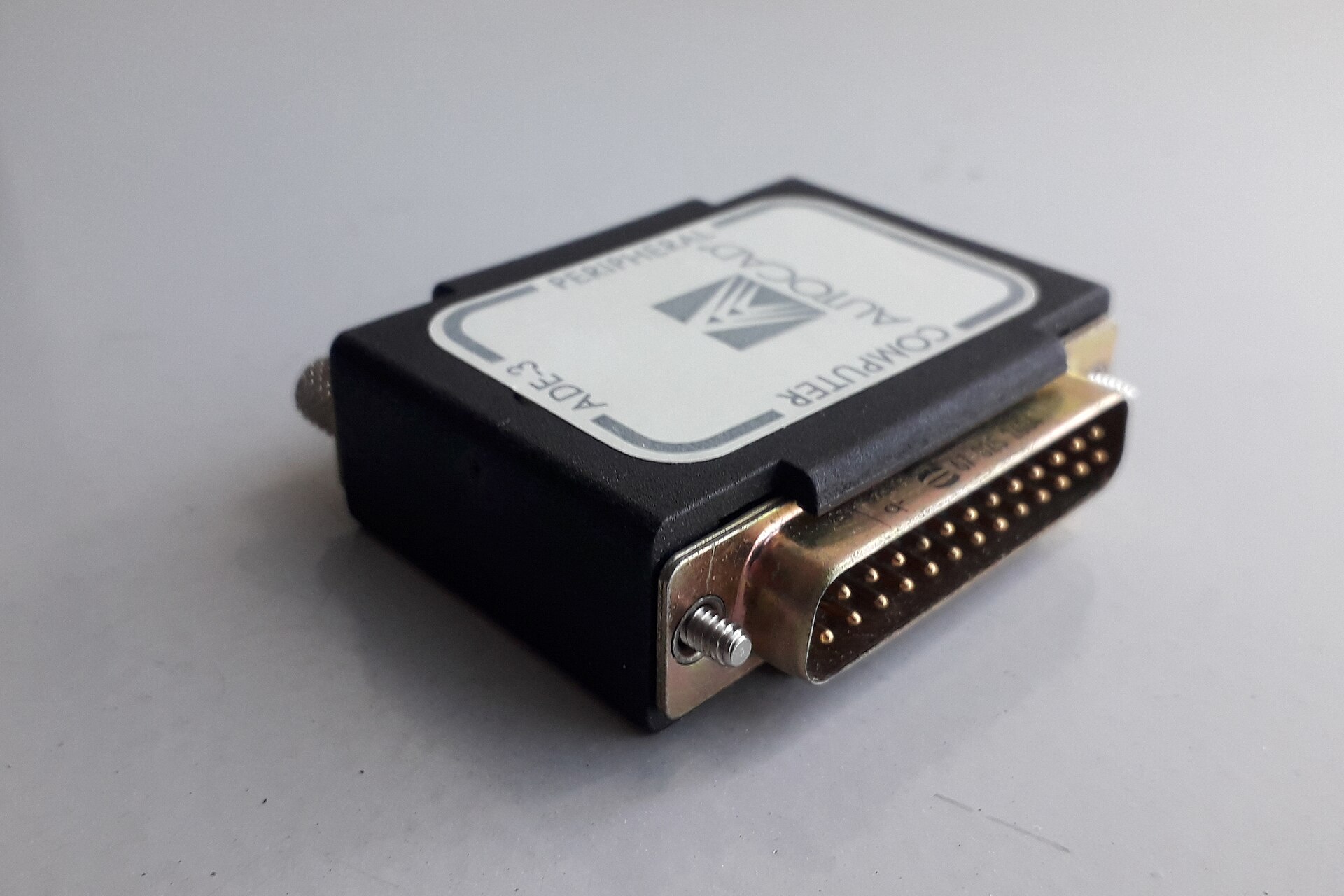 A black 1990 AutoCAD hardware lock with a 25-pin parallel port connector, lying on a white surface.