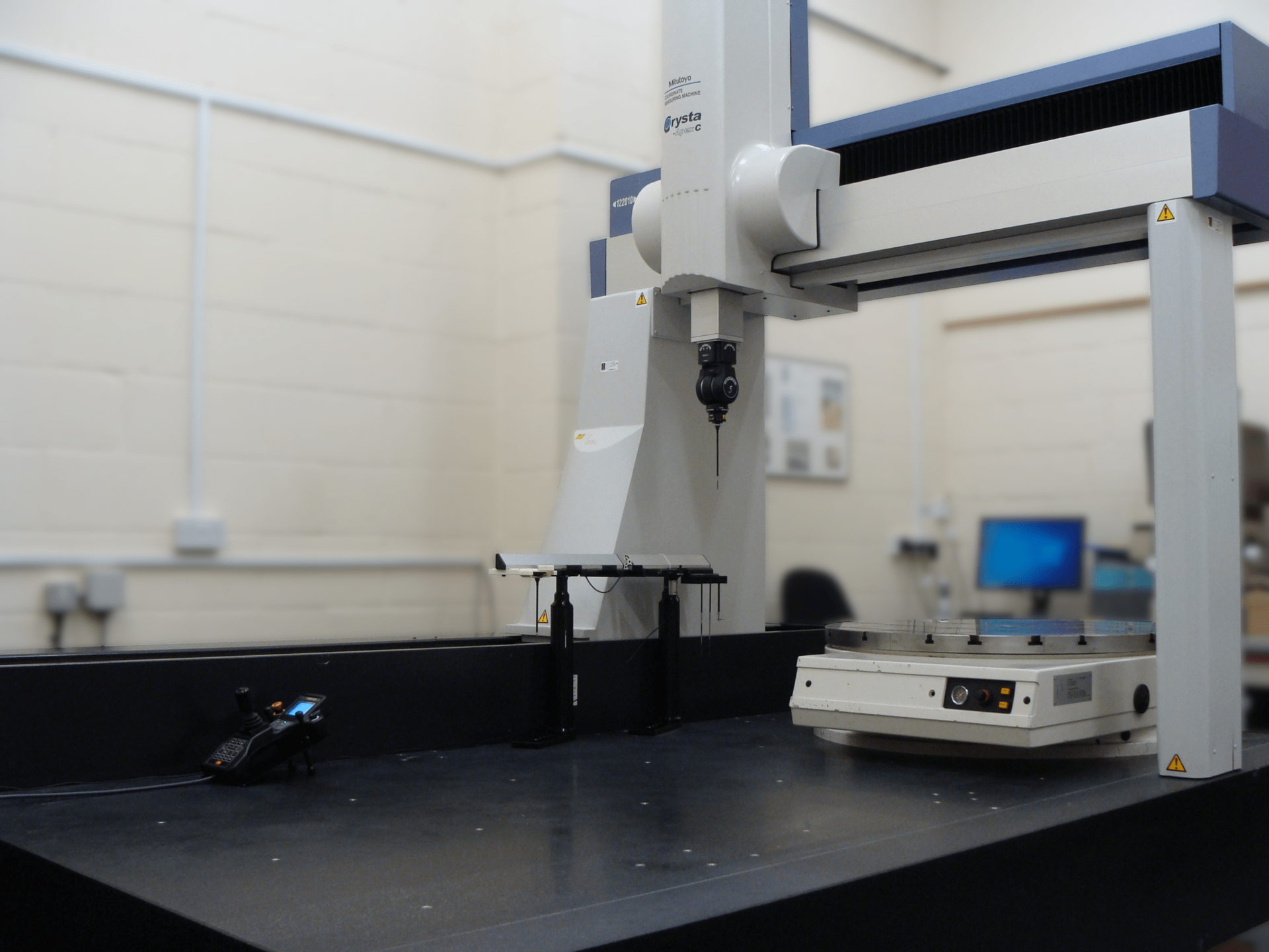 A bridge-style coordinate measuring machine with a scanning probe head over a granite table in a metrology room.