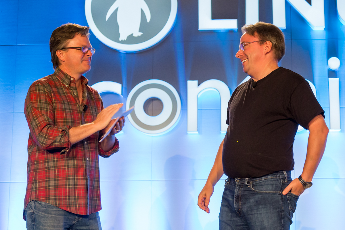 Linux creator Linus Torvalds and Linux Foundation executive director Jim Zemlin talking on stage in front of a large Linux Foundation backdrop.
