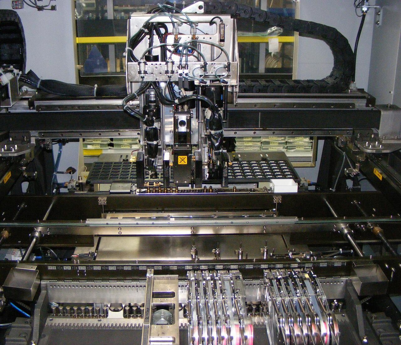 The gantry and placement heads inside a surface mount pick and place machine, above a circuit board.