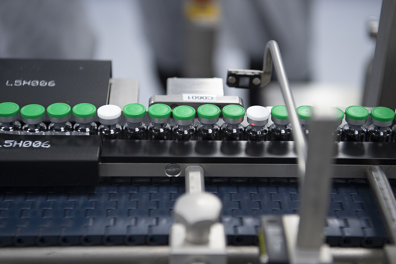 Close-up of a pharmaceutical fill-and-finish line with rows of green-capped vials moving through a machine.