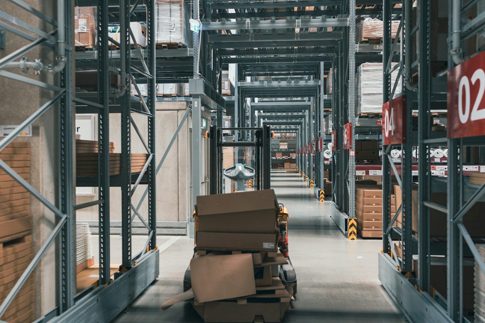 A large warehouse aisle filled with stacked boxes on shelves. Photo: Salah Ait Mokhtar / Unsplash.