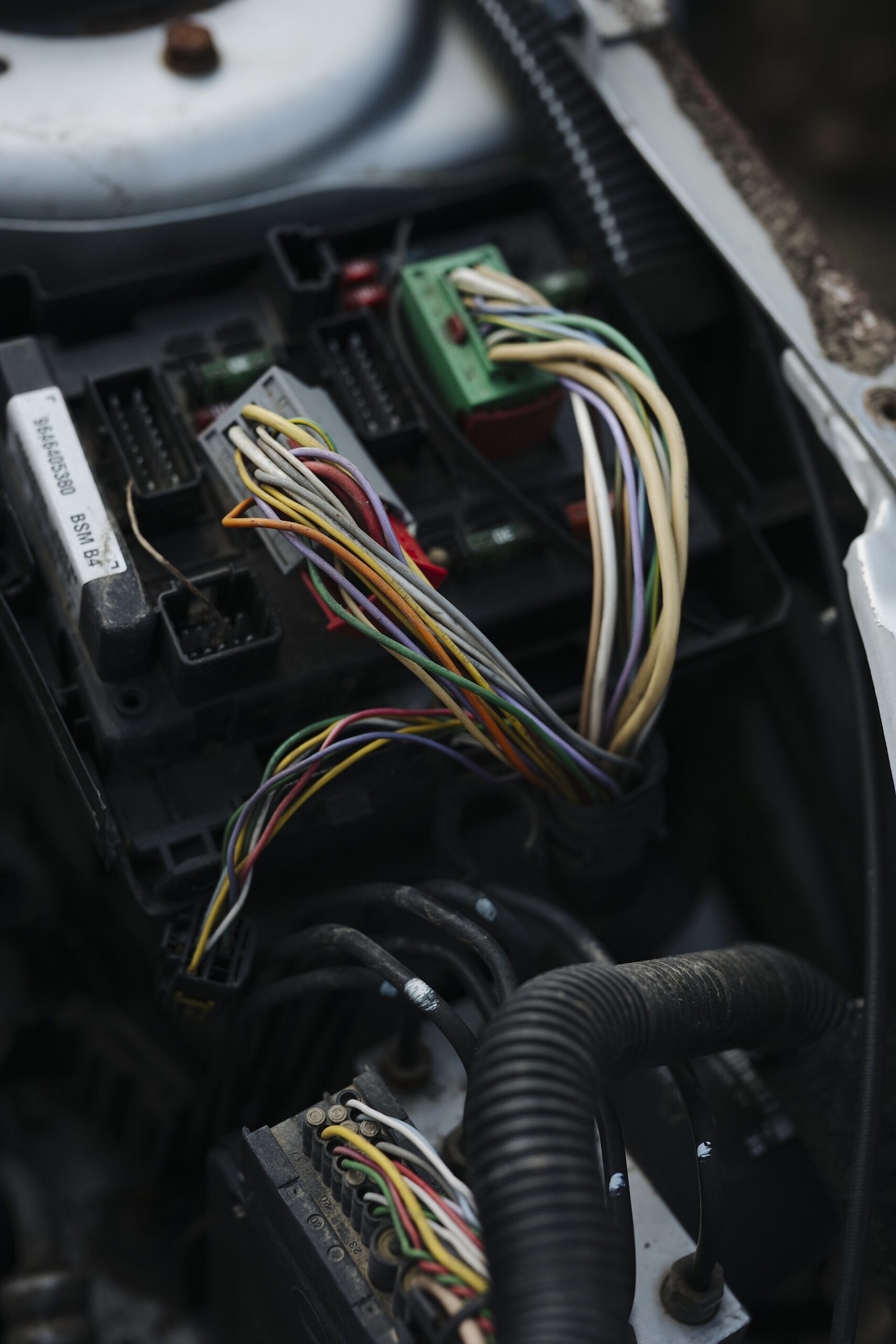 Bundles of colored wires plugged into an electronic control unit under the hood of a car during a repair.