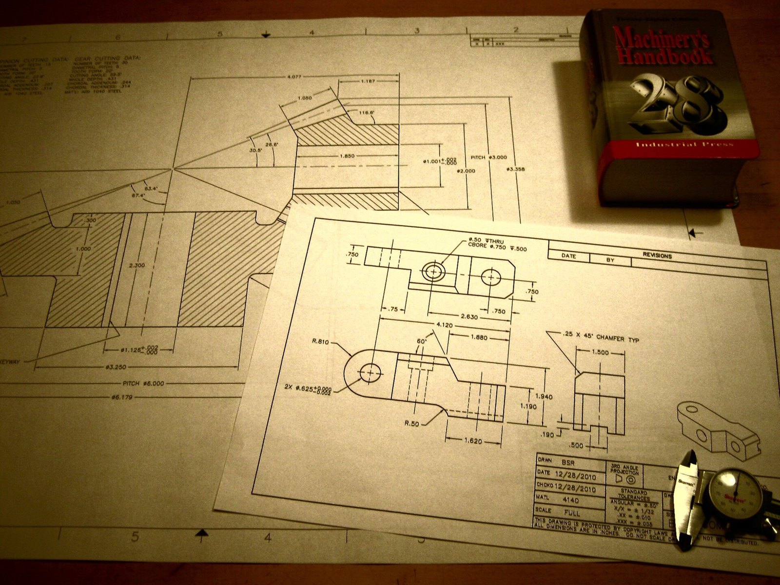 Engineering drawings of a bevel gear set lying beside a dial caliper and a copy of Machinery's Handbook. Photo: Benrobuck, CC BY-SA 3.0, via Wikimedia Commons.