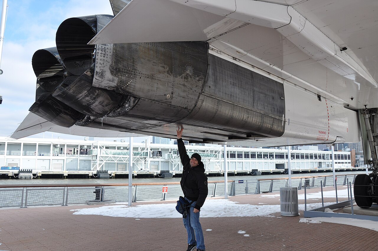 A person reaches up to the exposed hot section of a Rolls-Royce/Snecma Olympus 593 engine under the wing of a Concorde on display.
