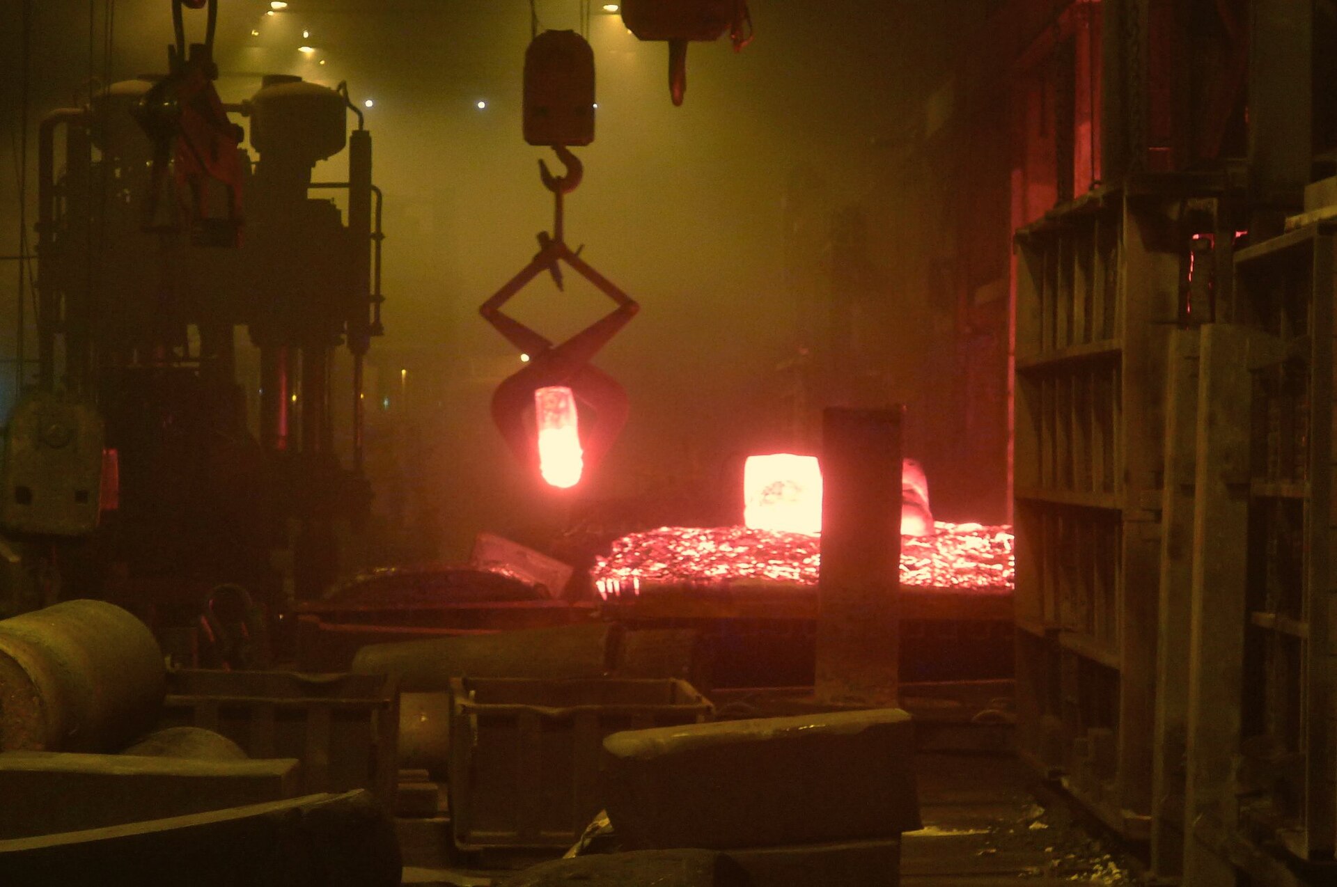 Glowing red-hot steel ingots, one hanging from crane tongs, inside the dim, smoky A. Finkl and Sons forge shop in Chicago. Photo: Seth Tisue, CC BY-SA 2.0, via Wikimedia Commons.