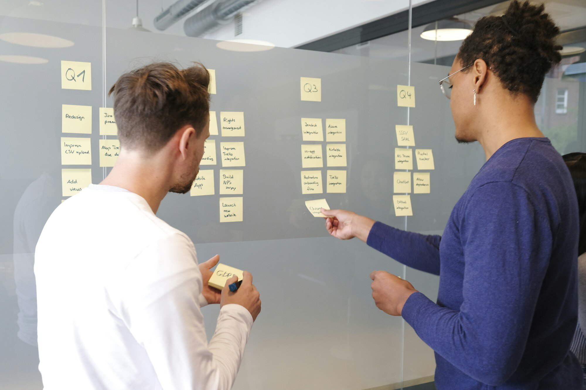 Hands arranging sticky-note cards on a kanban planning board—resource allocation and concurrent work without false conflicts. Photo: airfocus / Unsplash.