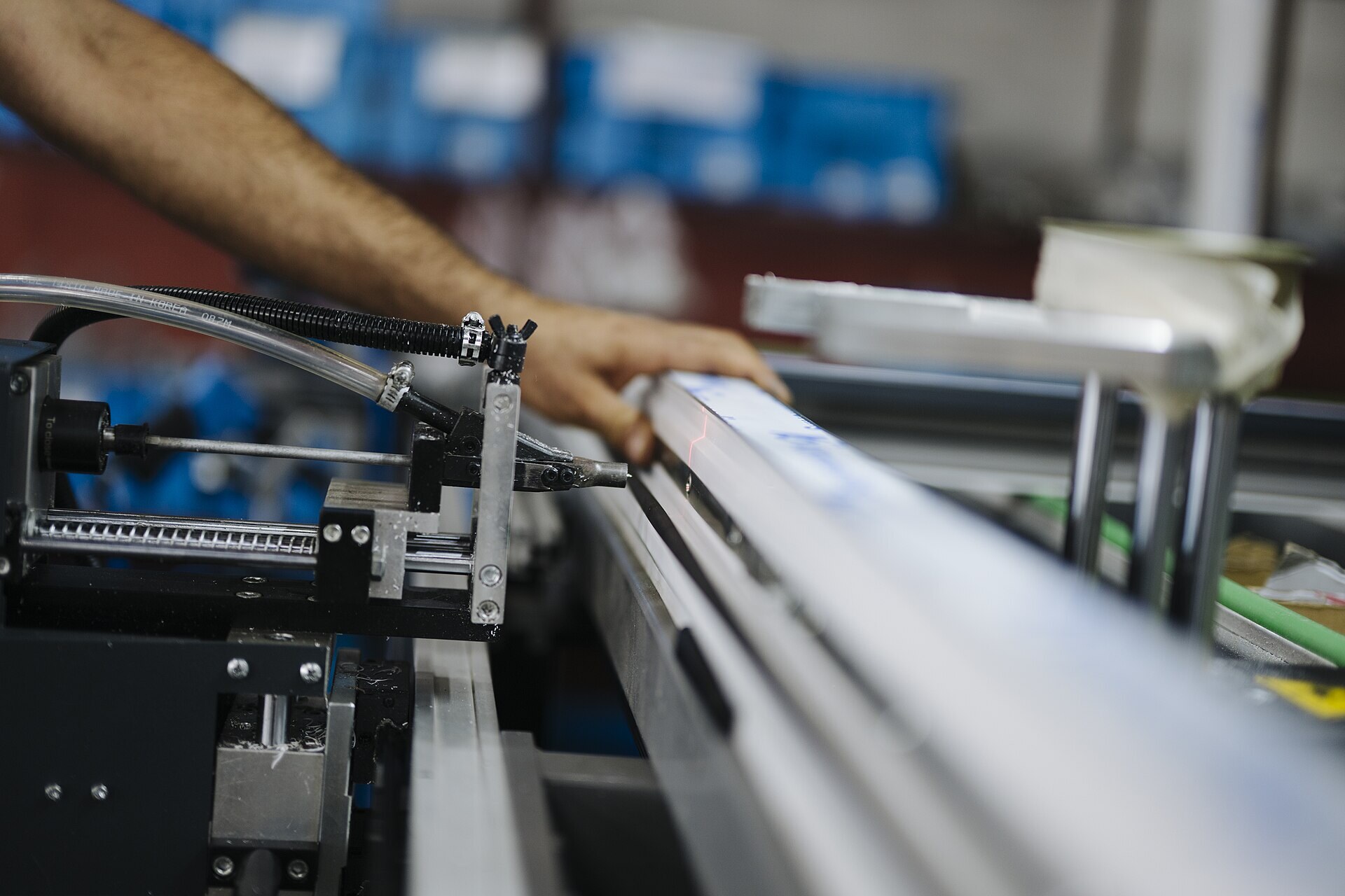 Operator guiding an aluminum extrusion under a red laser alignment line on a precision factory station—CapEx programs fund these line investments. Photo: Shixart1985 / Wikimedia Commons.