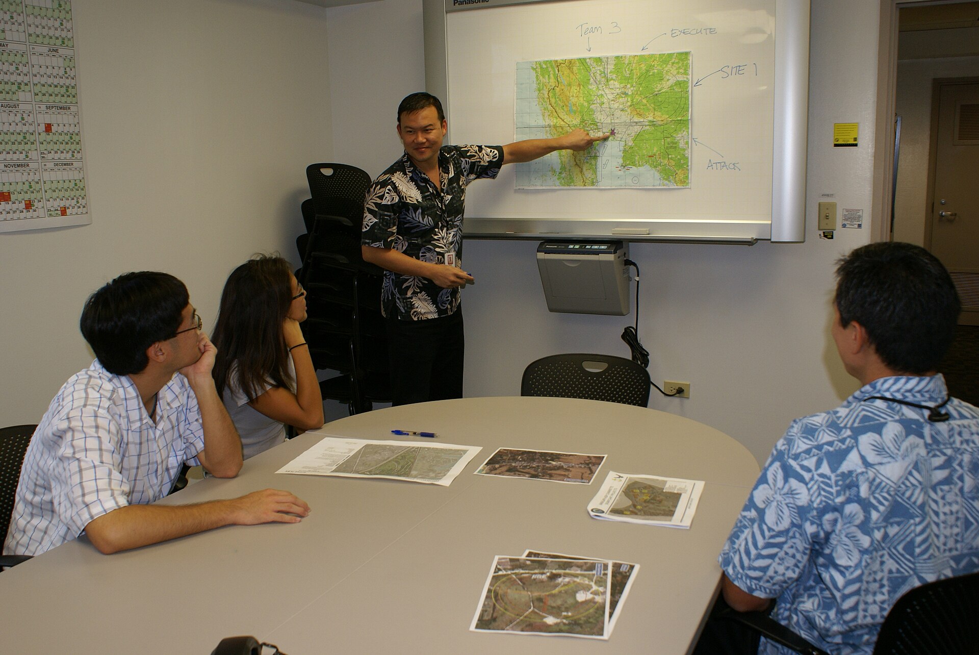 A NAVFAC Pacific supervisor runs the weekly Monday planning meeting with his Hawaii Planning Branch team around a conference table. Photo: NAVFAC, CC BY 2.0, via Wikimedia Commons.