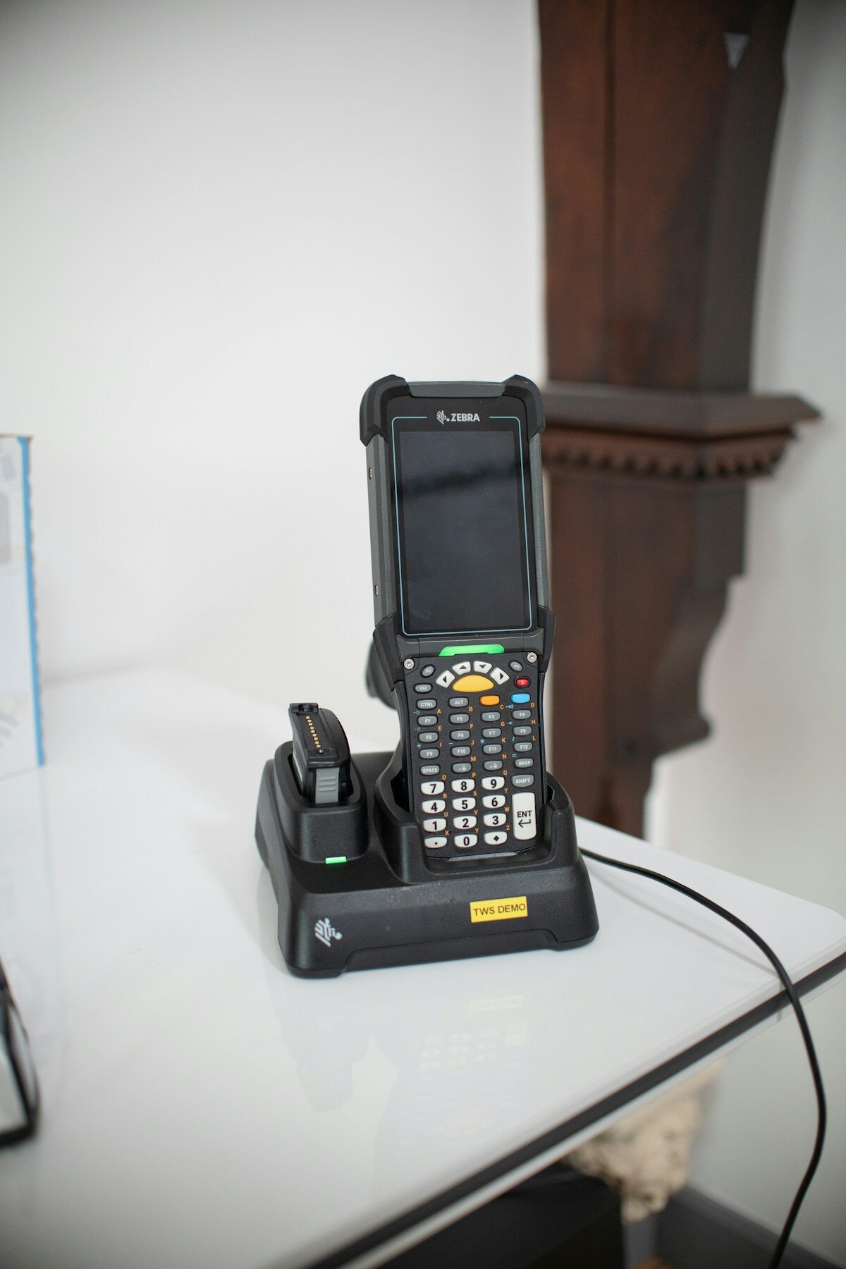 Rugged handheld barcode terminal docked in a charging cradle on a workbench