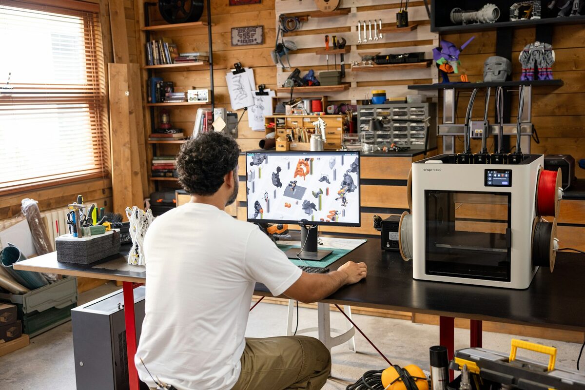 Maker at an engineering desk working in CAD beside a desktop 3D printer