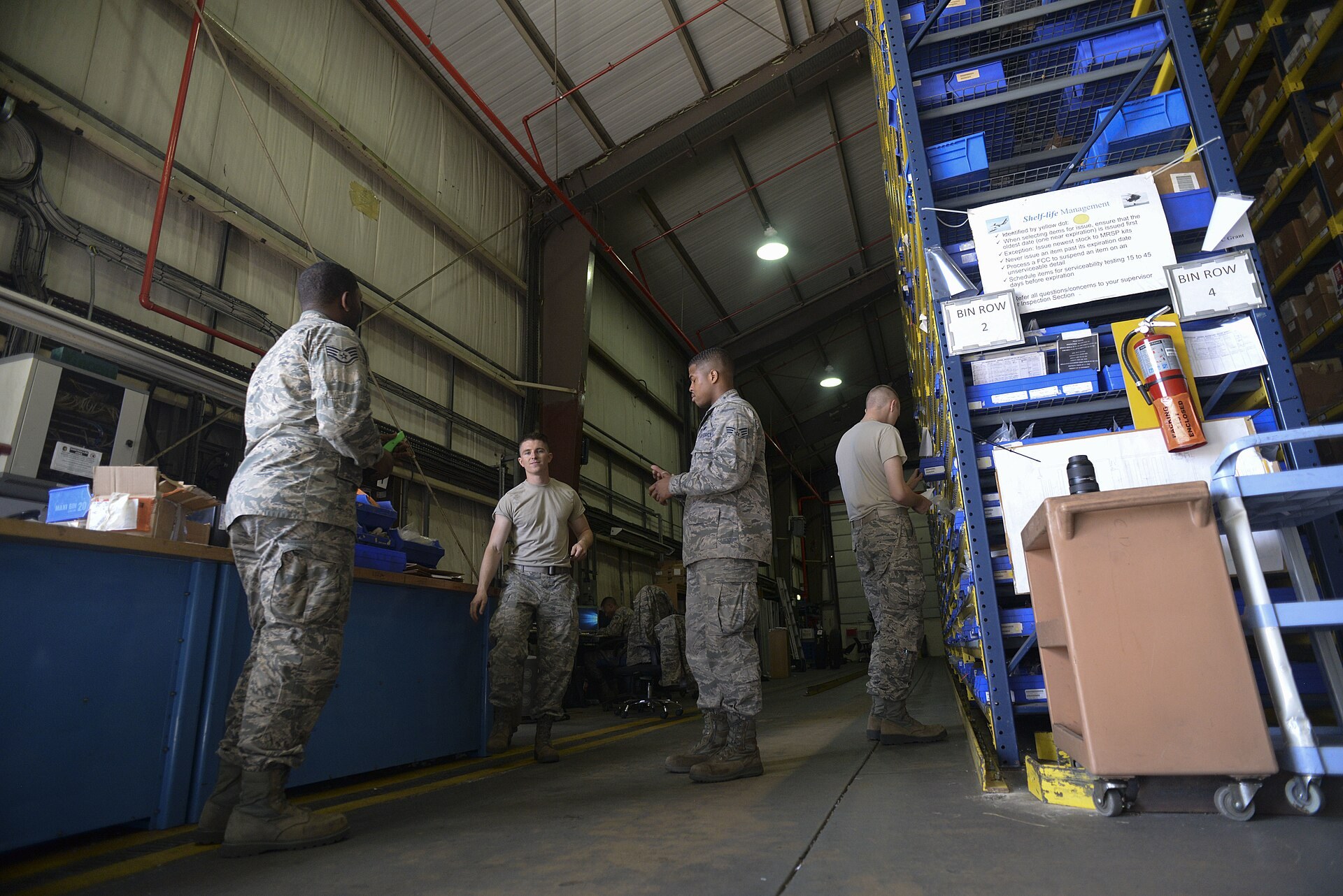 Airmen at an end-of-day briefing in an aircraft parts store warehouse