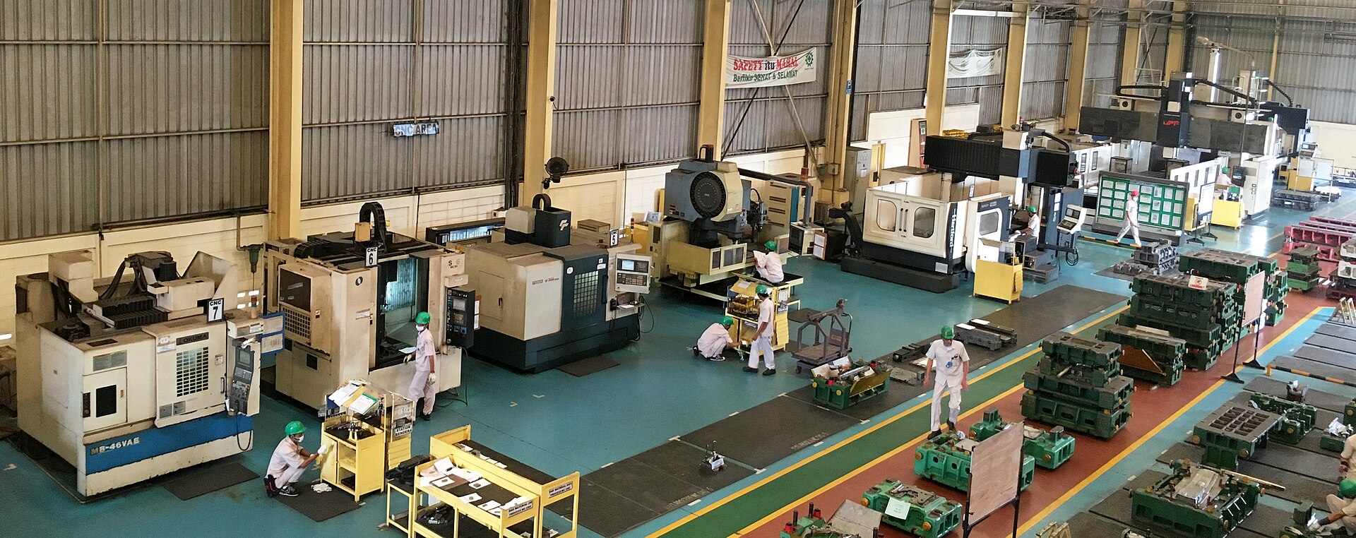 Wide view of a CNC machining floor at PT Metindo Erasakti in Indonesia, with machining centers lined up along the wall and workers in green hard hats. Photo: Antoniusaw, CC BY-SA 4.0, via Wikimedia Commons.