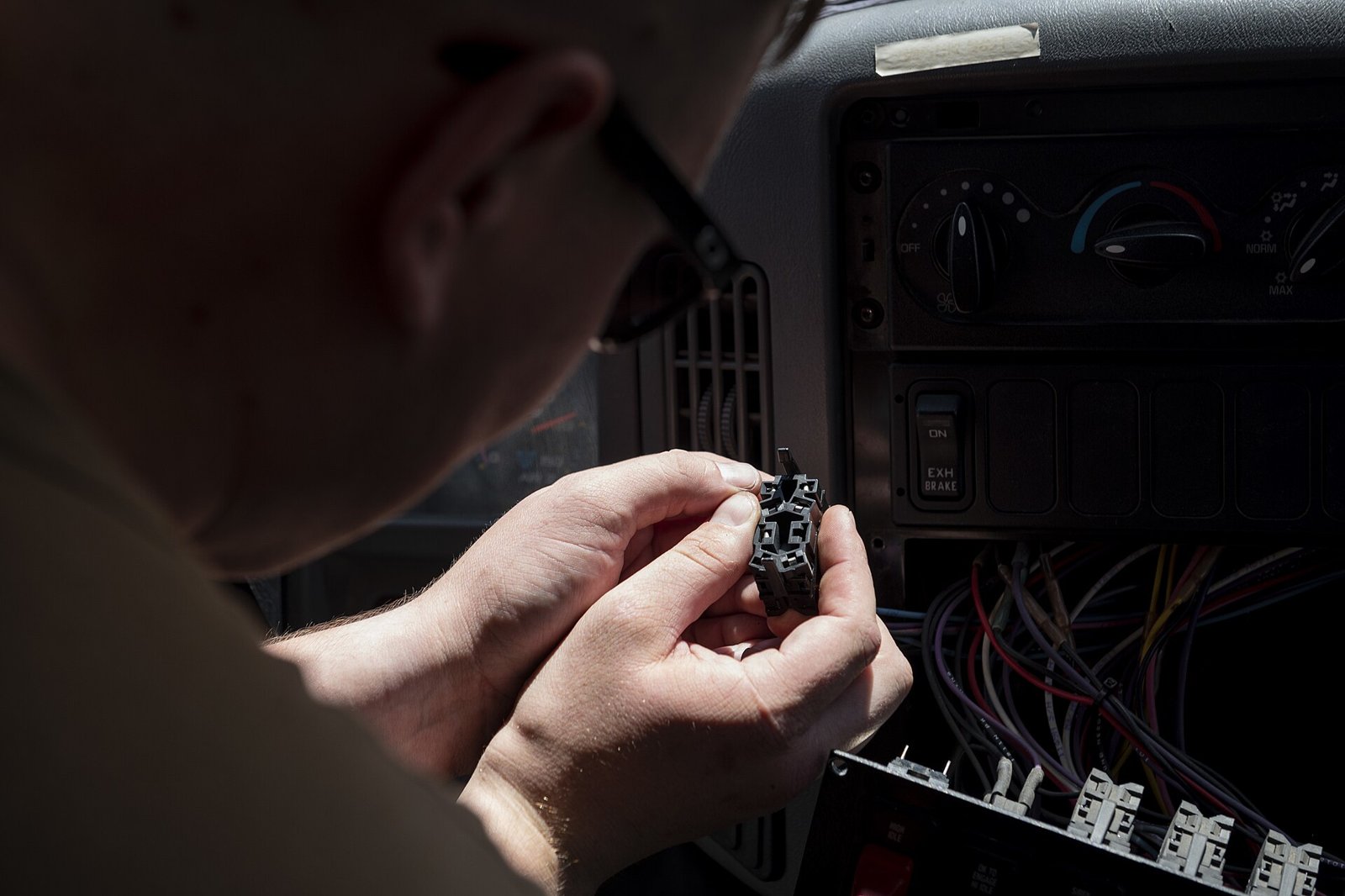 A Navy construction mechanic holds a relay socket in front of an open dashboard panel and wiring on a structural fire truck. Photo: U.S. Navy / Petty Officer 2nd Class Brianna Green, public domain, via Wikimedia Commons.