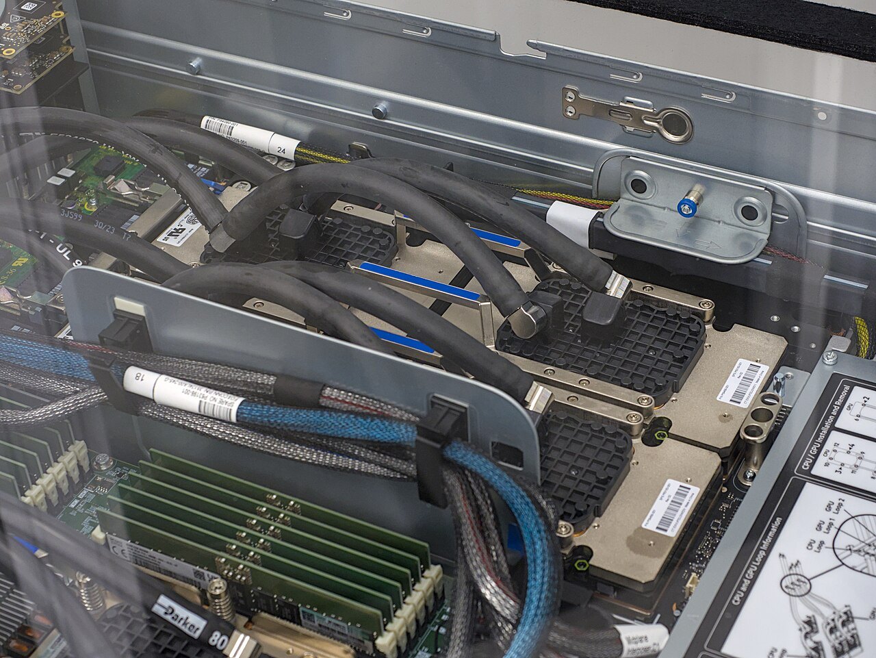 Inside a supercomputer node: four NVIDIA H100 GPU modules under blue and black liquid-cooling hoses, next to rows of memory modules.